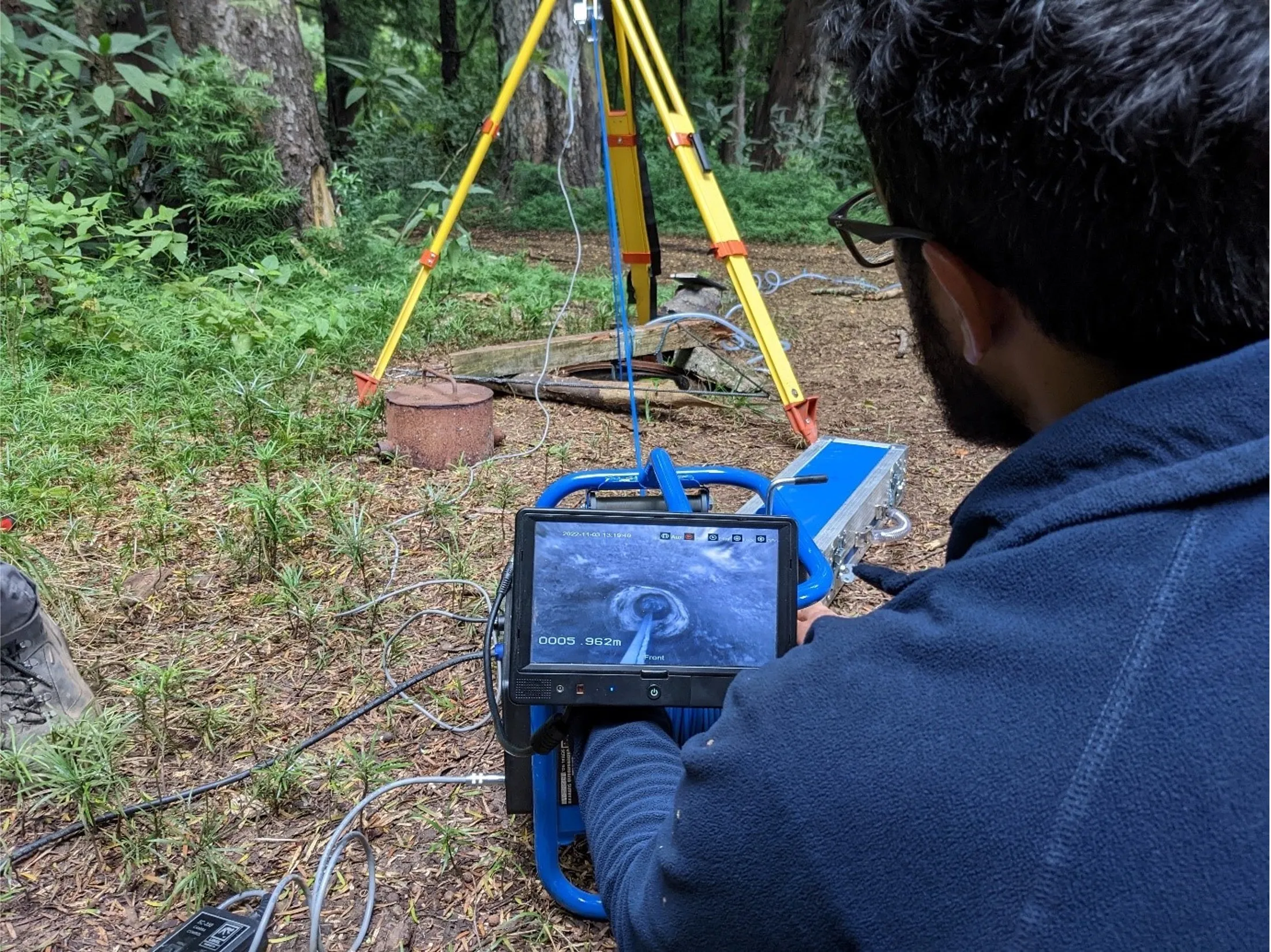 Pictured in a wooded area, a person assesses a camera with yellow bracketing equipment in the background.
